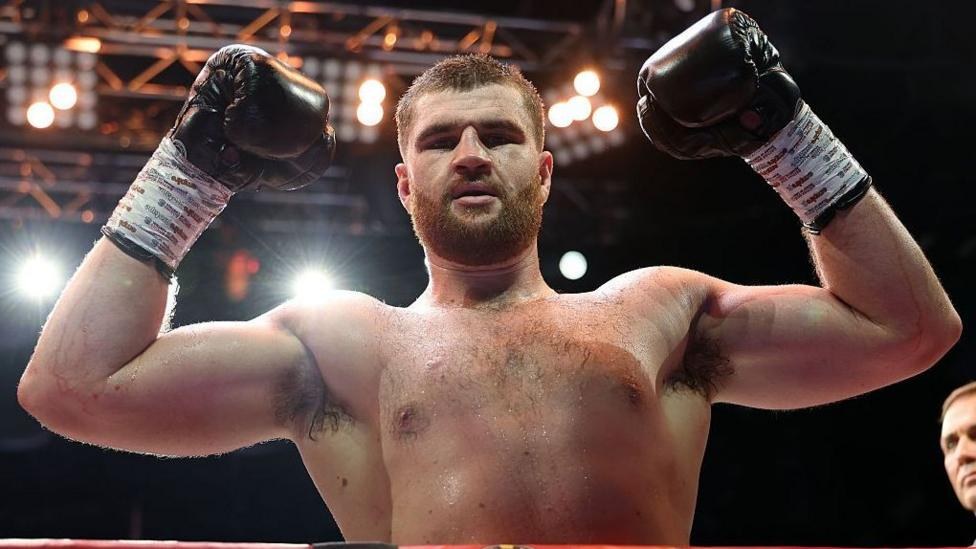 Johnny Fisher holds up his arms and is wearing boxing gloves